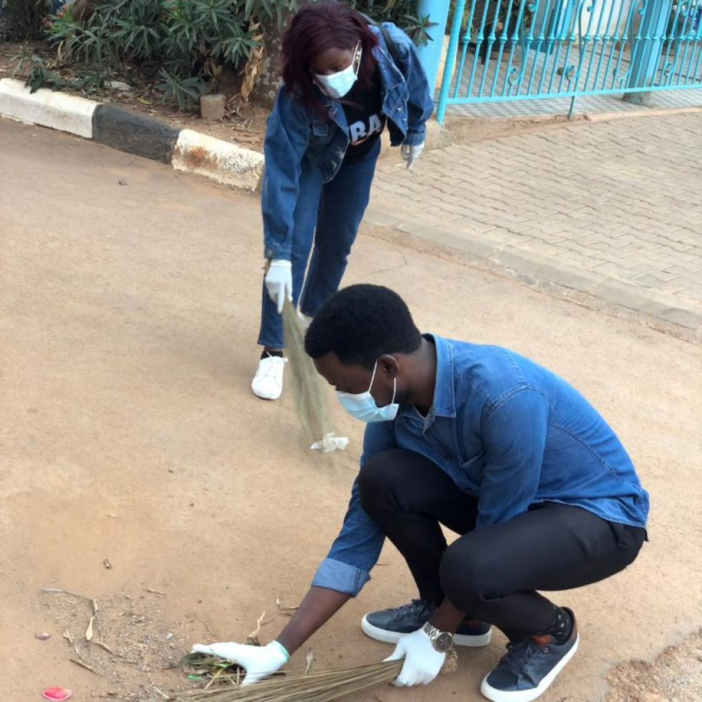 Two Learnwell Initiative volunteers sweeping litter from a roadside in Nansana